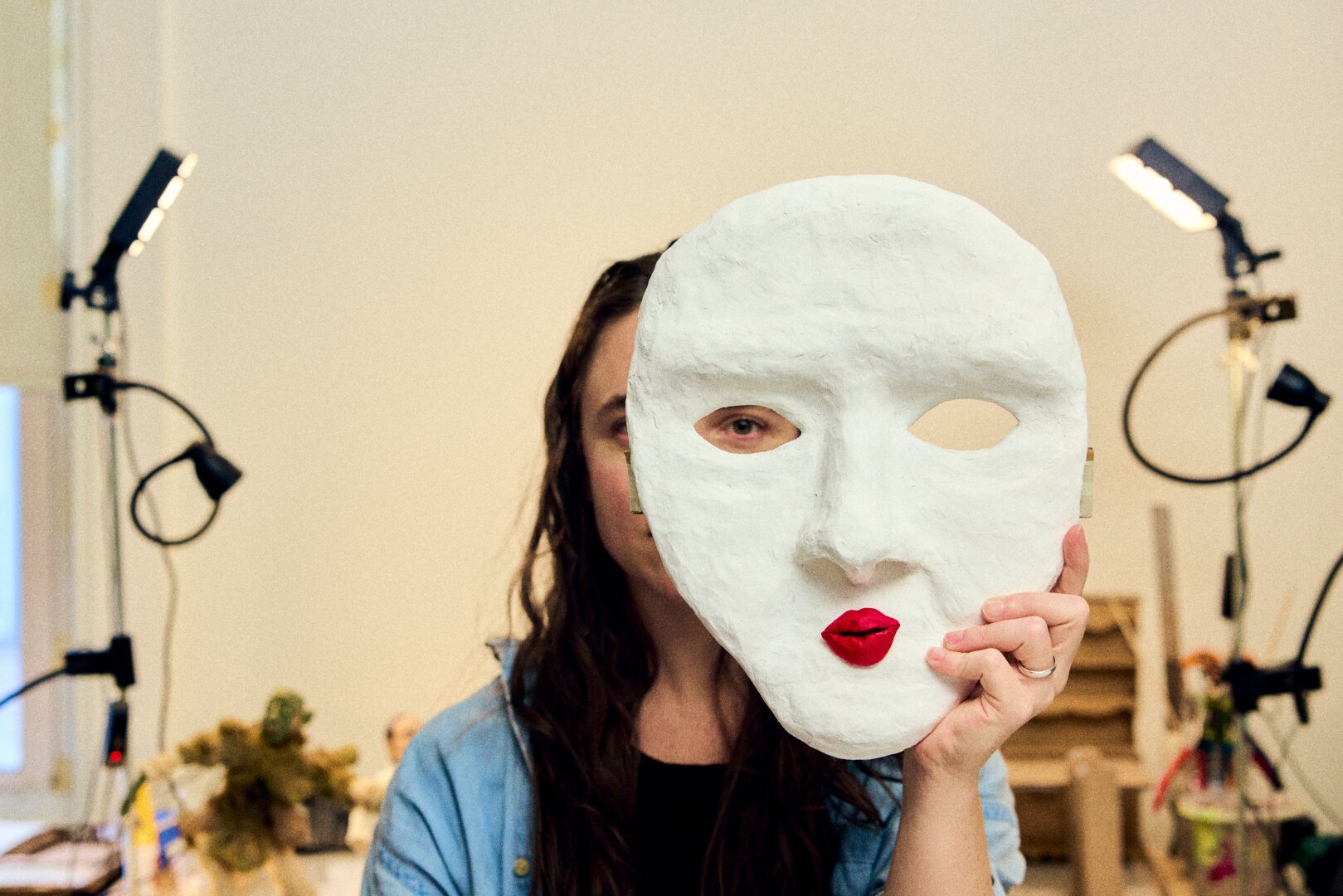 An artist looks through one eye of a clay mask