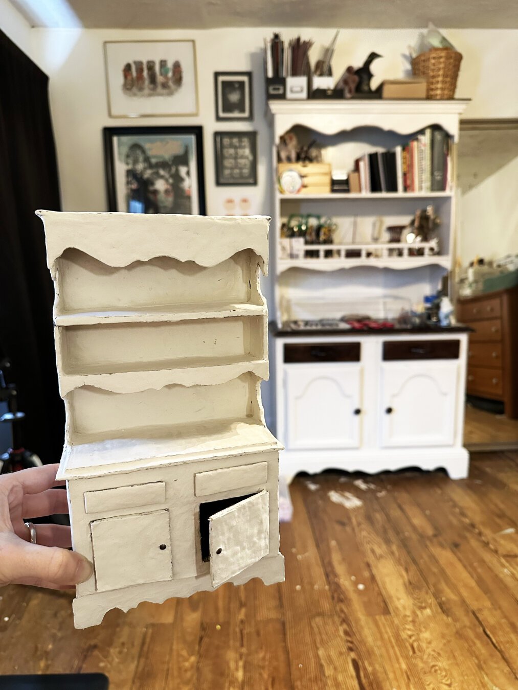 A hand holds a miniature hutch with the life size hutch in the background