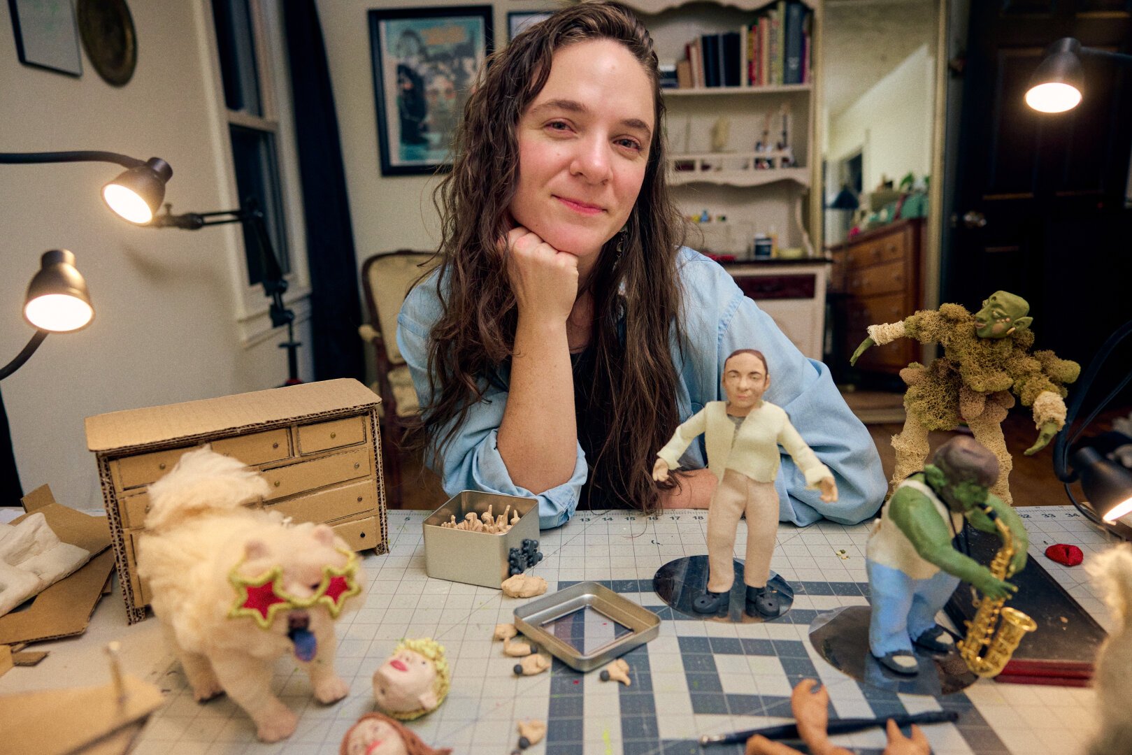 Artist poses in art studio with claymation and stop-motion puppets