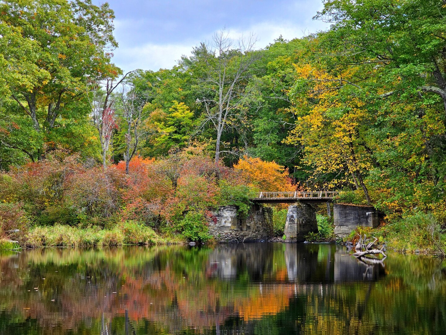 A shot of a old stone bridge in the autumn season, with the foliage starting to really pop. The vibrant color of the leaves and structure of the bridge is reflected in the river water.
