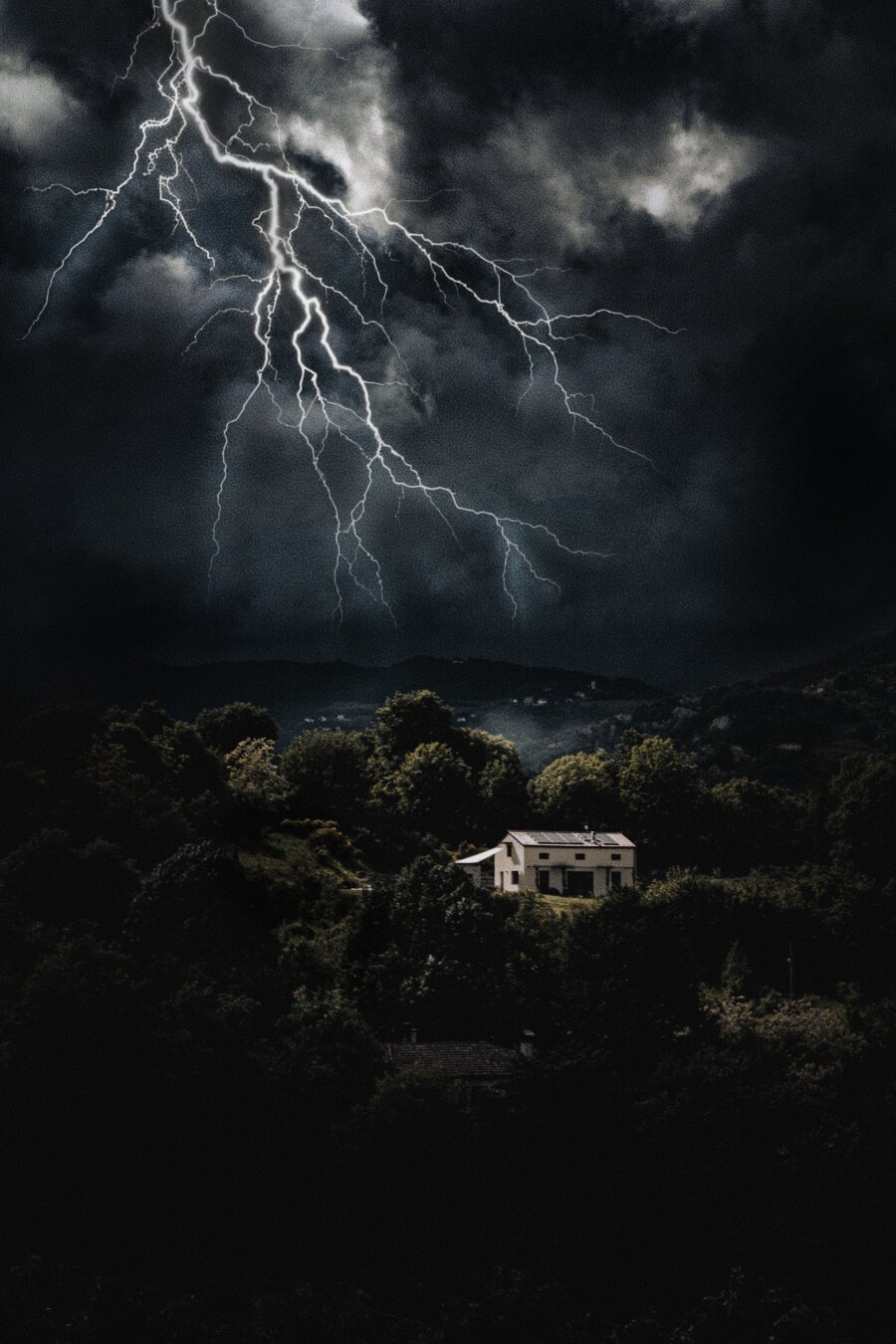 This is a composite/double exposure (the lightning is just a free png the rest is mine). There is a  large bolt of lightning which branches across dark storm clouds in the upper left of the photo. Below the stormy sky there's a white house which is nestled among a dense, dark forest of trees on hills.