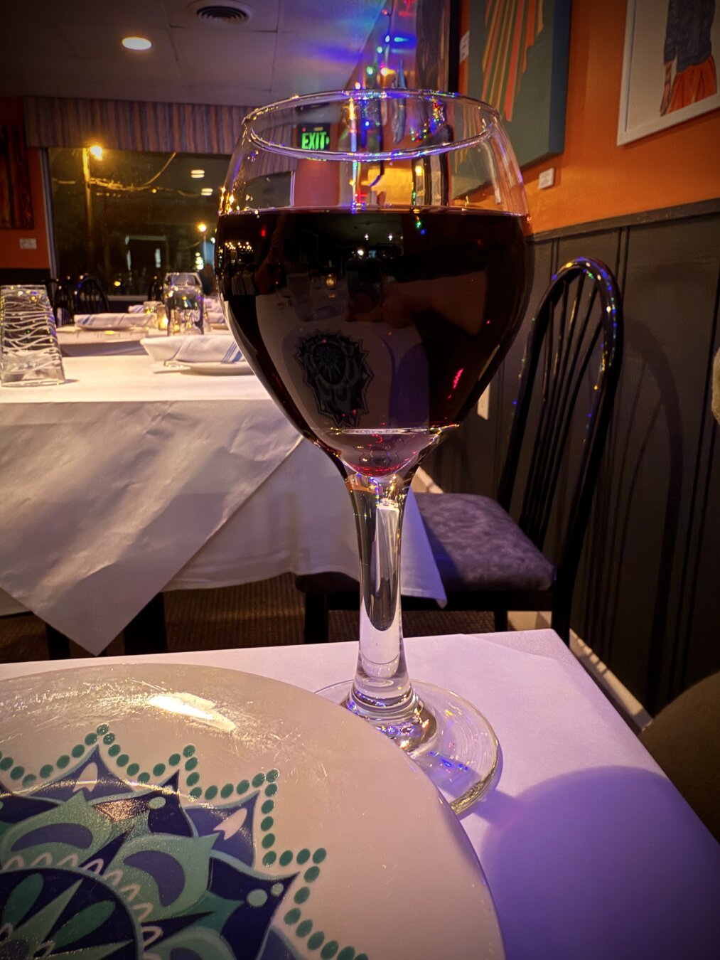 Close up of red wine in a glass in front of an eclectic artistic wall.