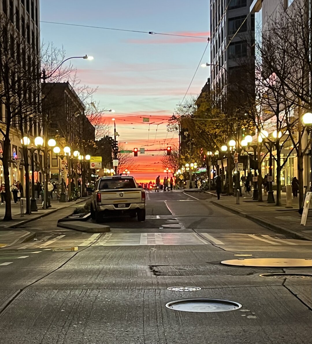 A vivid sunset sky centered between rows of brightly-lit downtown shops, the lights of Pike Place Market just barely visible down the hill three blocks to the west.