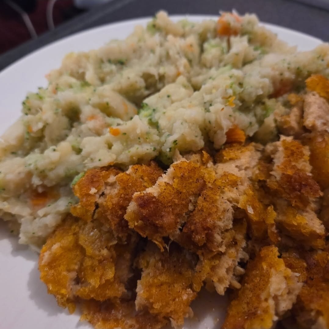 A plate of food showing a serving of mashed vegetables—likely including potatoes, carrots, and broccoli—next to crispy, breaded pieces of what appears to be a plant-based schnitzel or cutlet. The dish looks warm and hearty, with a home-cooked feel.