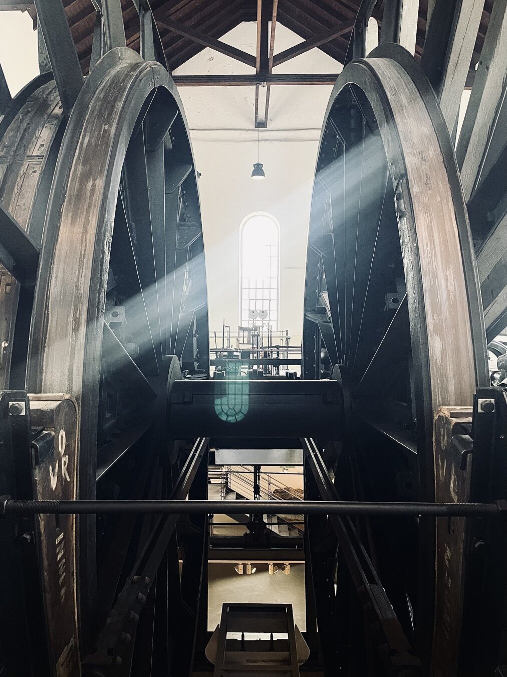 It is a photograph taken at the museum Zeche Nachtigall in Witten. You See the the back of a winding engine. It is a view between the big wheels to an windows at the back of the room.