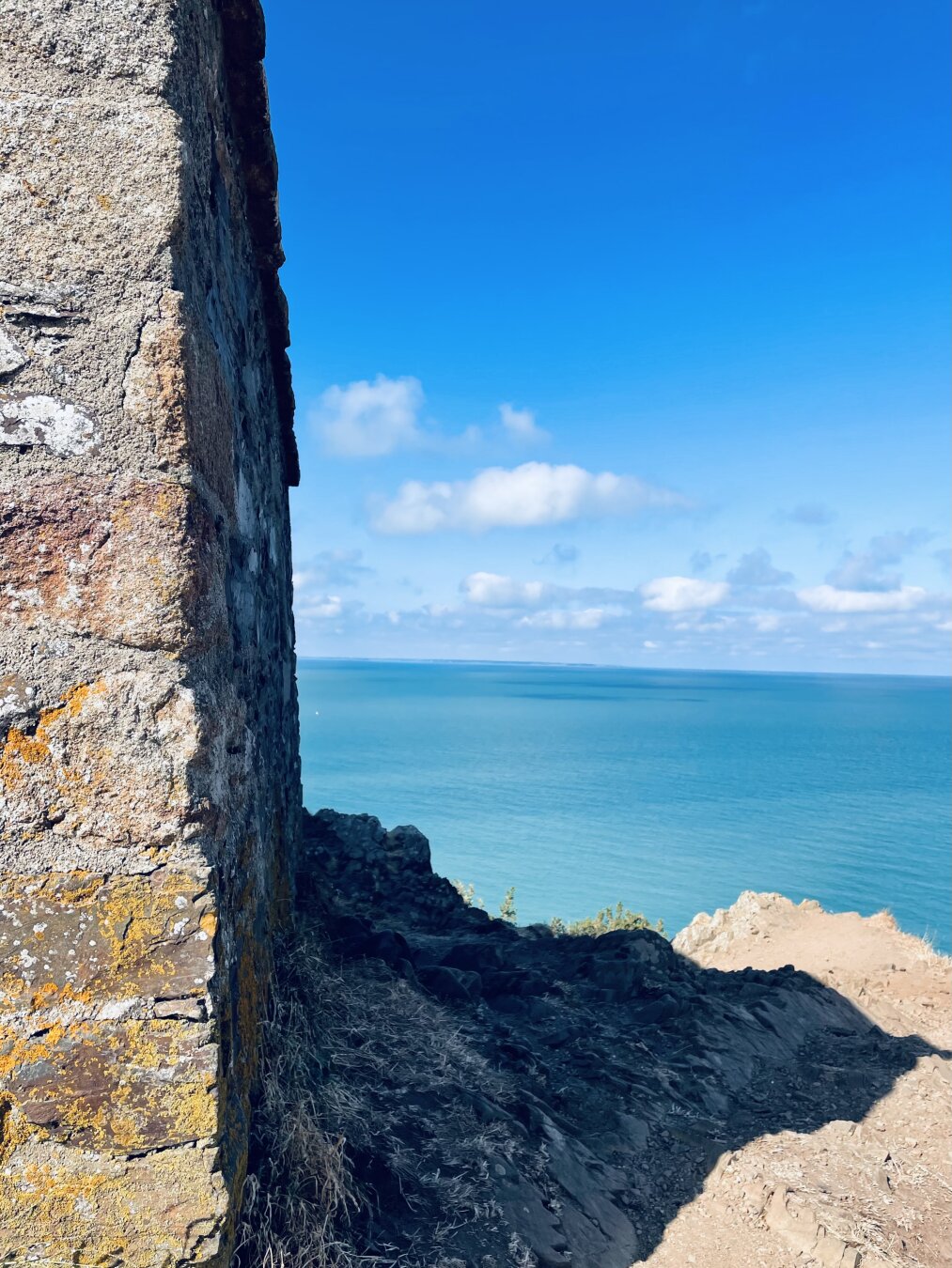 You see a color photograph. It shows the side wall of the caban vauban at Carolles in the Normandy. Thwo-thirds of the pictures is a view beside this wall on the ocean and sky.