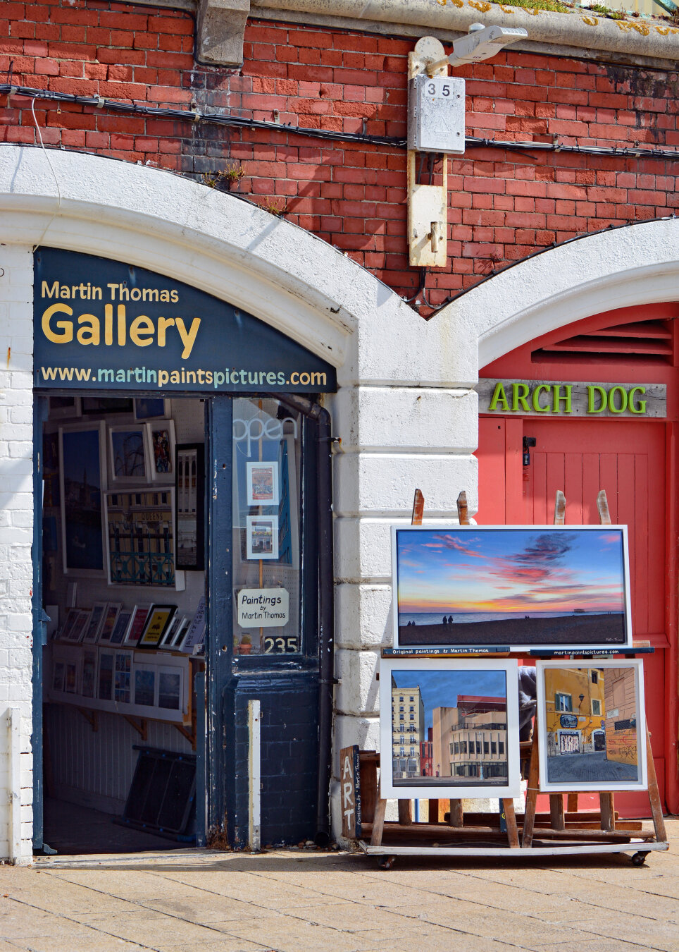 Photo of an art gallery situated under the King's Road arches in Brighton. There are some paintings displayed outside on easels.