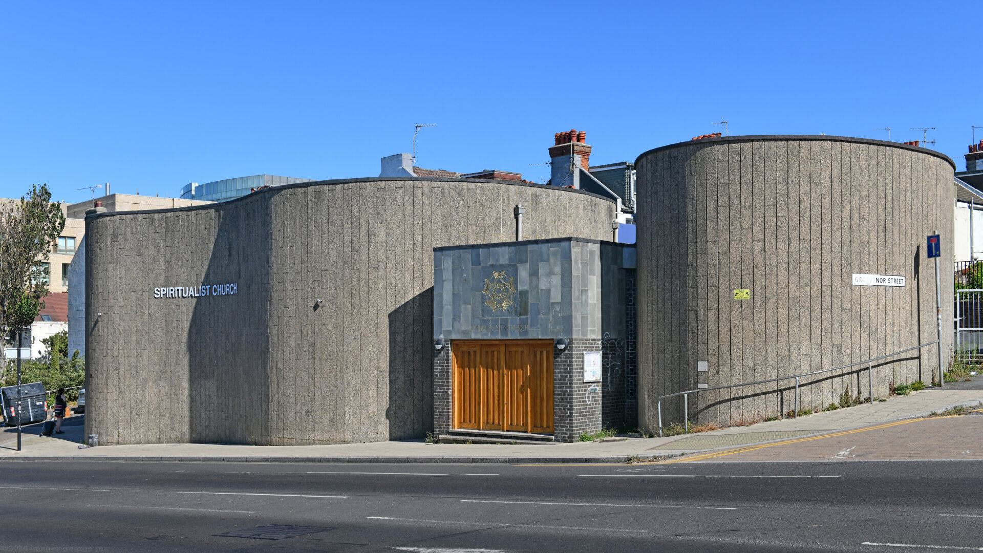 Photo of a Spiritualist church designed in the Brutalist style by Overton & Partners, 1965. A curving, windowless structure finished in shuttered concrete. Locally listed as a "good example of a modern design of place of worship". City of Brighton & Hove.