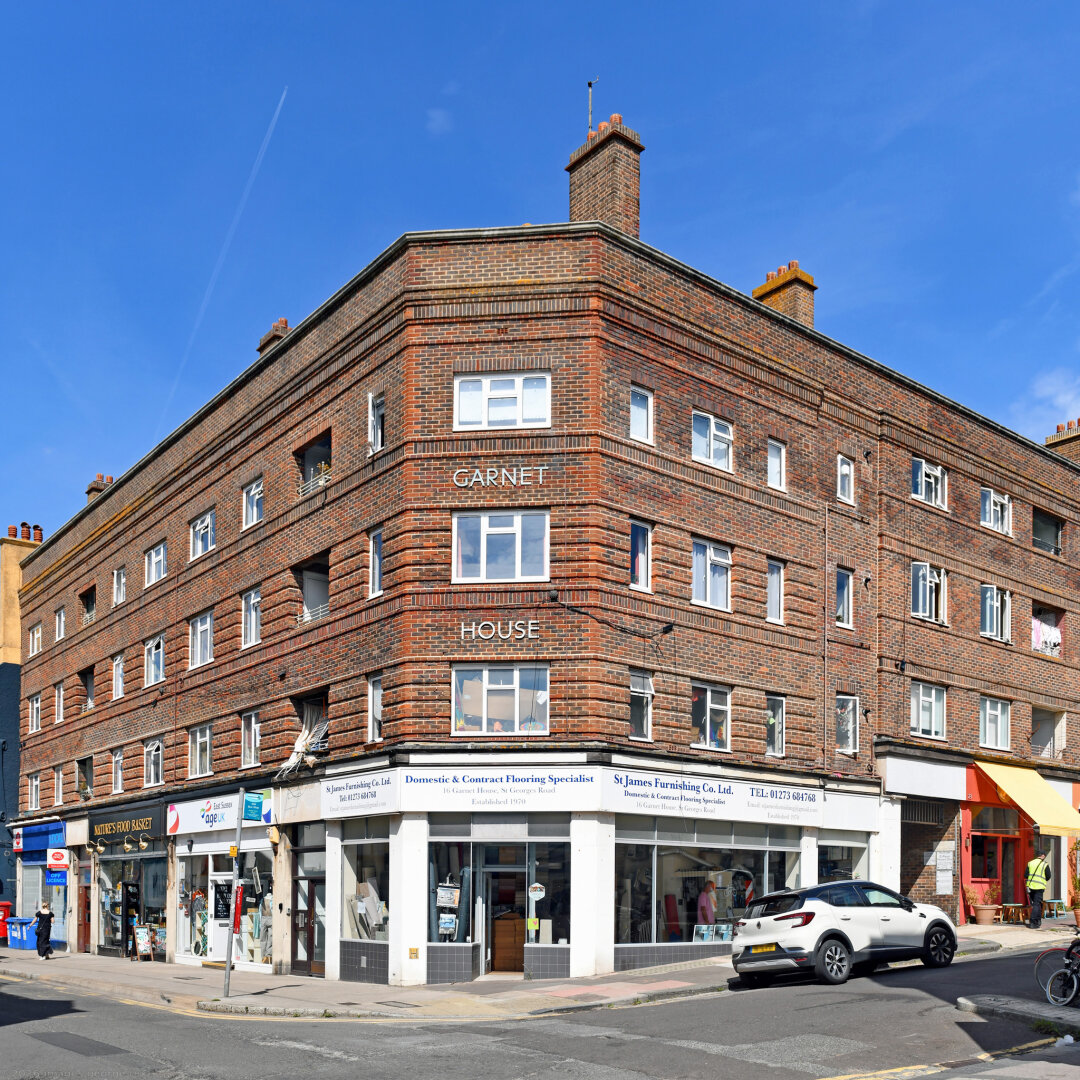 Photo of Garnet House in Kemptown. Red brick, four storeys, residential over ground floor retail.