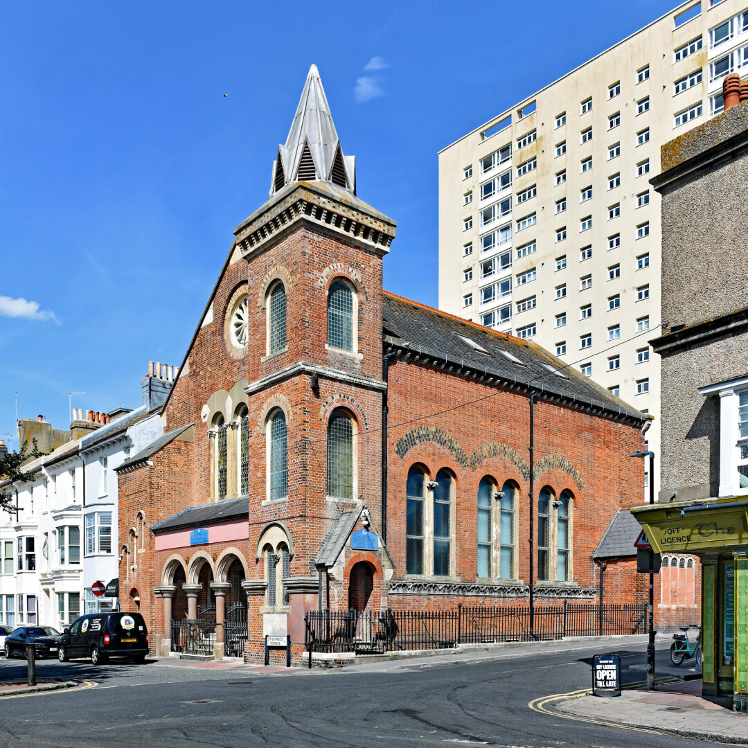 Photo of a former Methodist church in Kemptown designed by Thomas Lainson, 1873, using English bond brick and stone dressings. Slate roofs, tower lead clad. Style described as a High Victorian adaptation of Italian Romanesque. Grade 2 listed and now owned by Brighton College. Montague Place, City of Brighton & Hove.