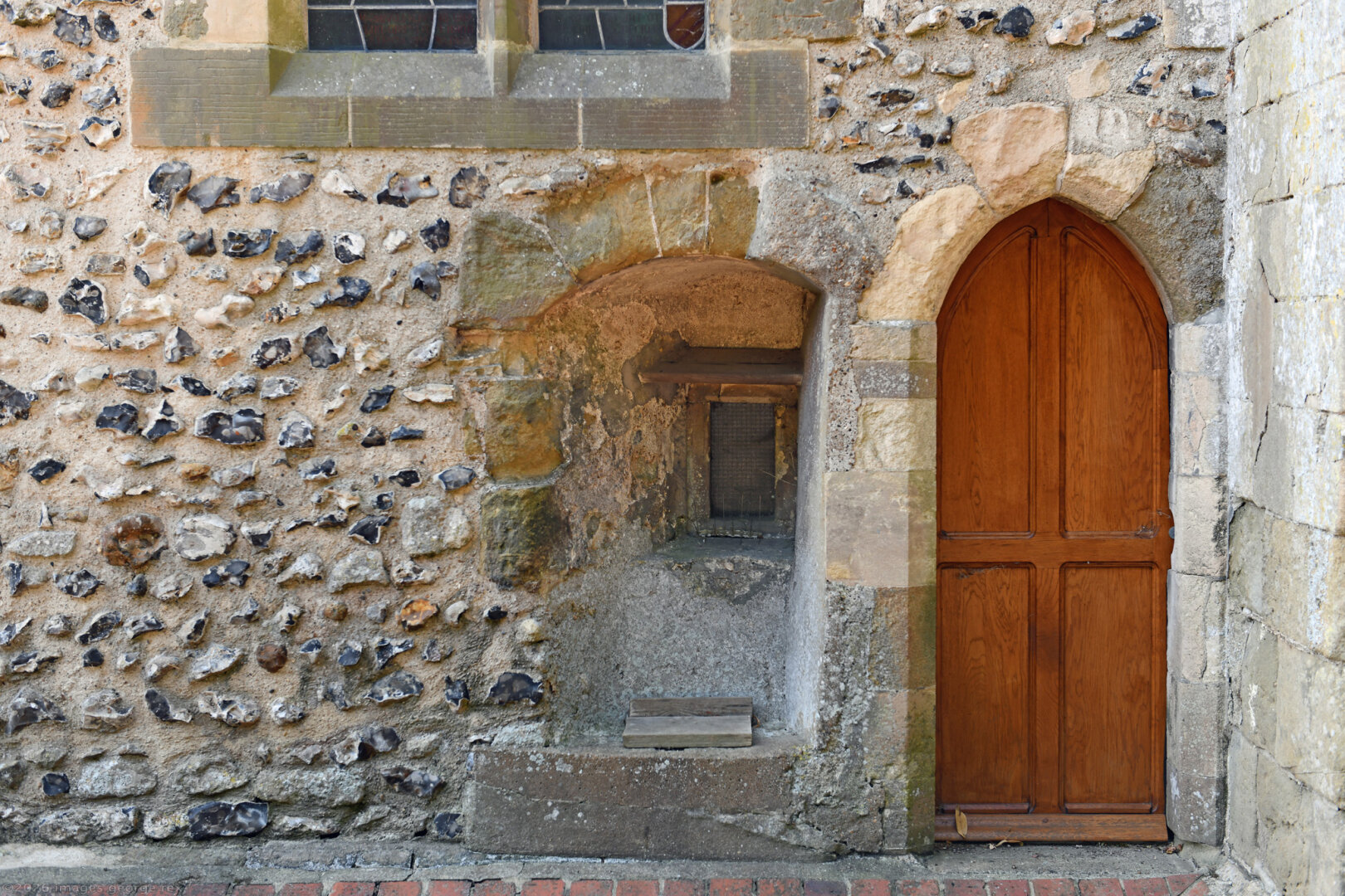 Detail showing the hagioscope, or squint, next to the north doorway of the Grade 1 listed church of St Julian. This feature is dated to the early fourteenth century and assumed to once have been connected to an anchorite's cell. Kingston Buci, West Sussex, UK.