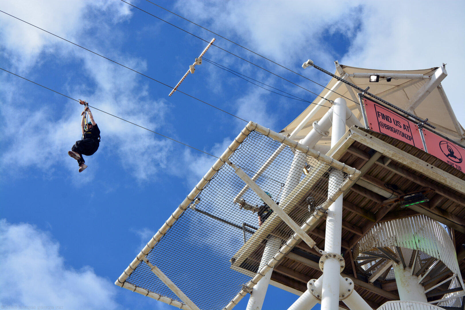 Photo looking up at the thirty metre, tubular steel Zipline tower on Brighton beach. Someone has just set off down the wire.