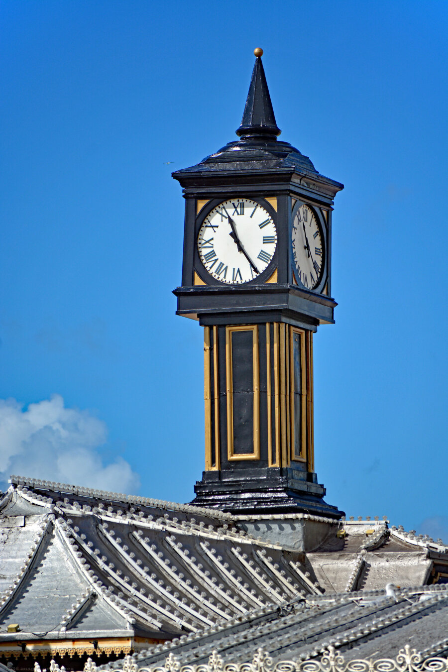 Photo of the Palace Pier clock tower of 1930, recently refurbished. Made of steel and timber cladded in zinc, painted black with gold-coloured detailing. The entire pier is Grade 2* listed. City of Brighton & Hove, UK.