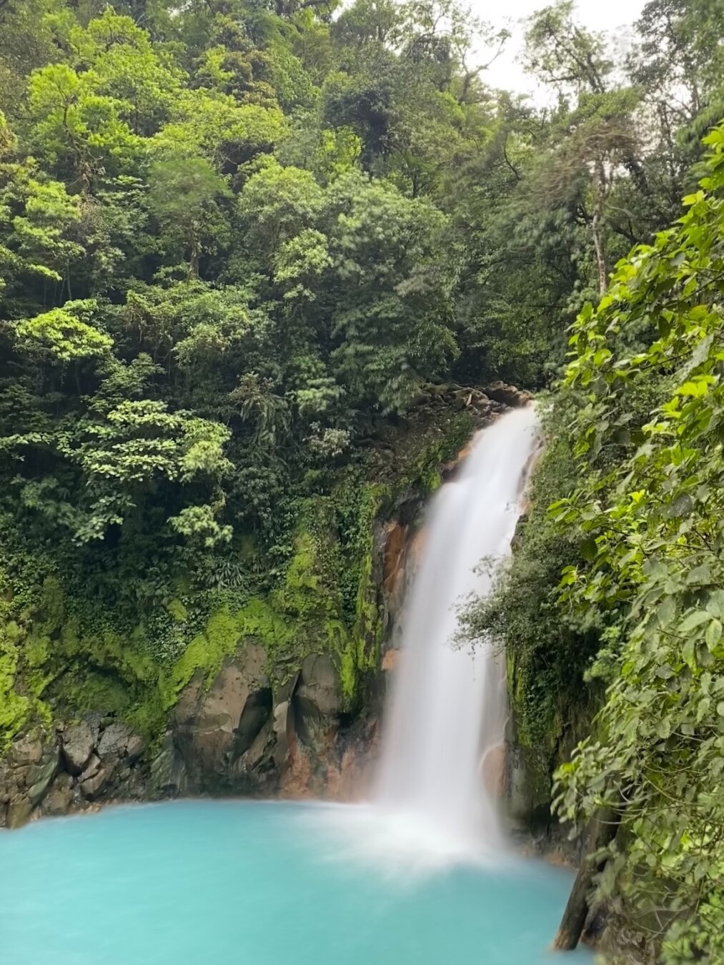 A long exposure picture of a waterfall falling into a saturated light blue pond