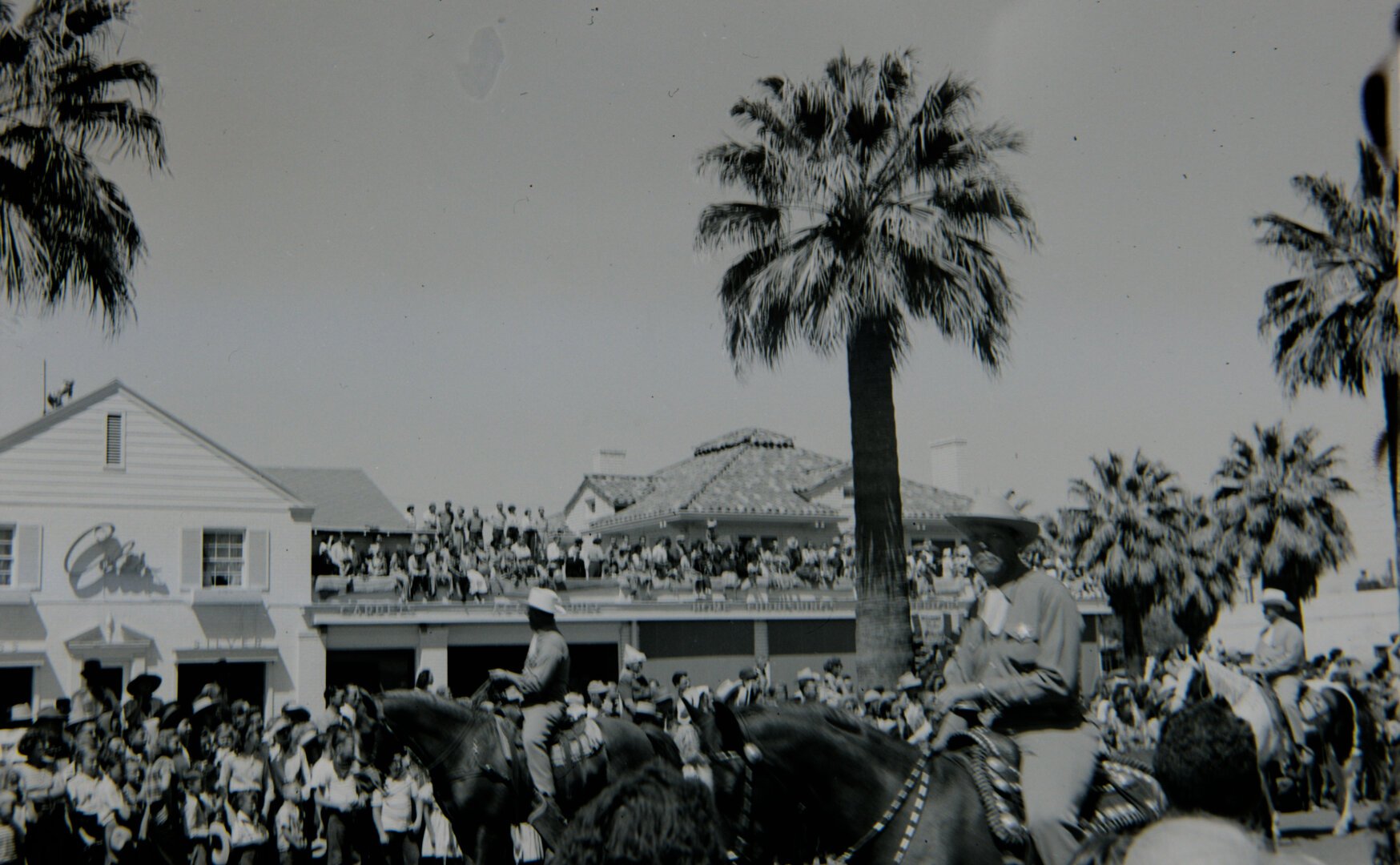 A crowd of people watches a parade. Men on horses are passing by