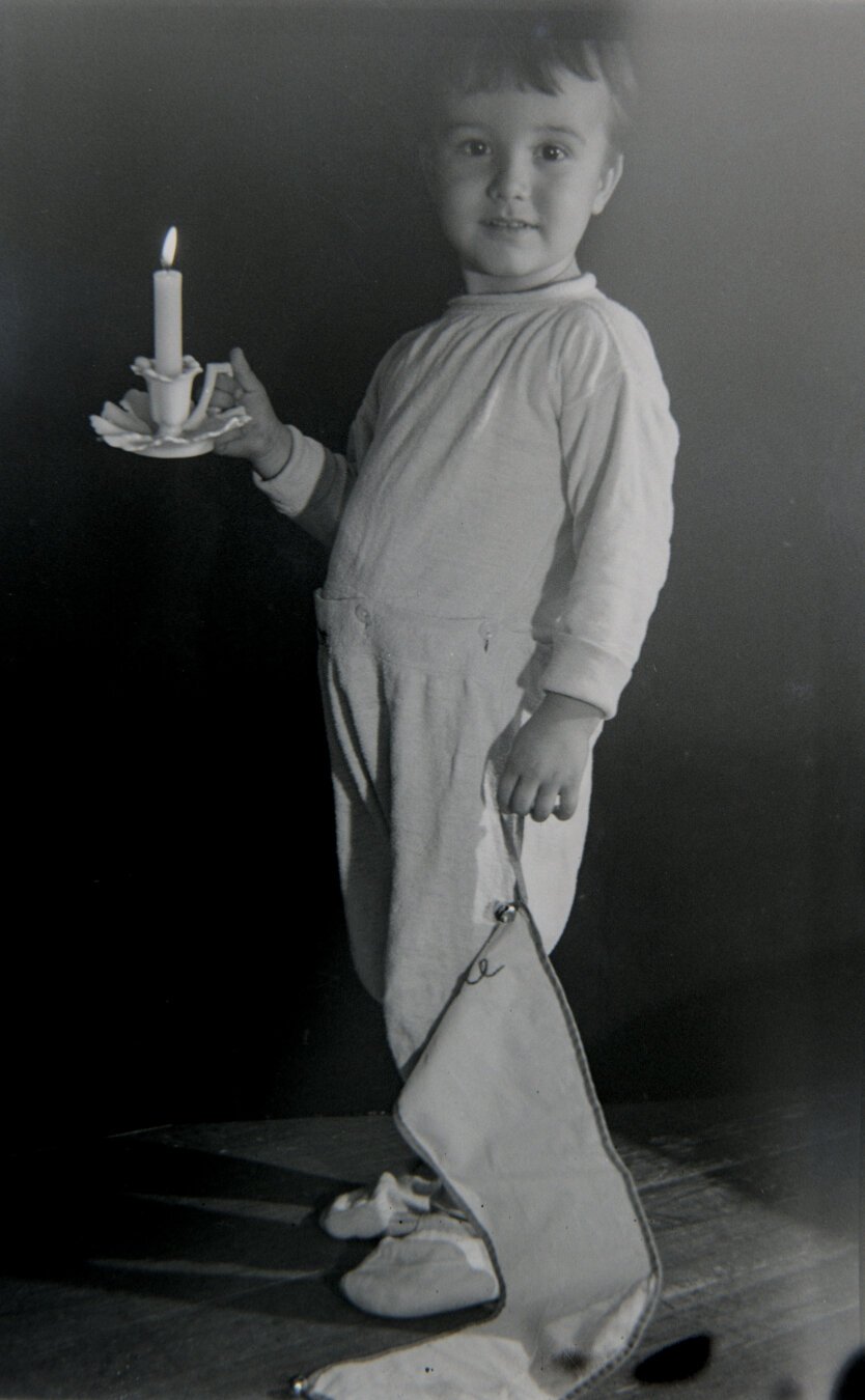 A young boy wearing pajamas and holding a candle and a Christmas stocking