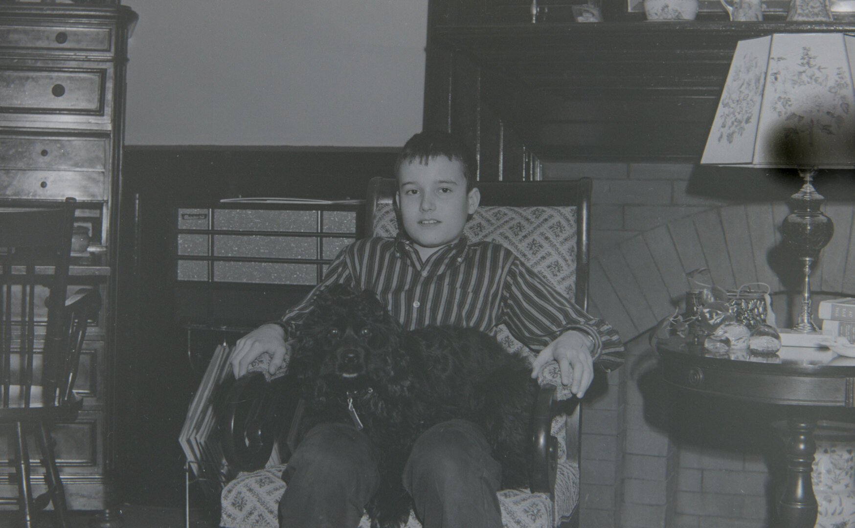 A young boy, looking very serious, sits in a chair with a black dog in his lap