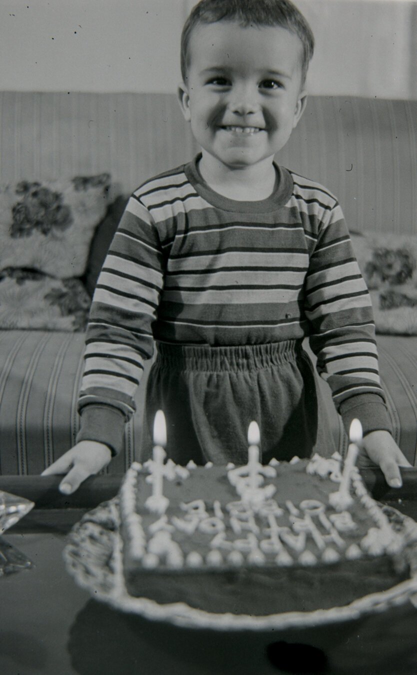 A young boy stands over his birthday cake, grinning