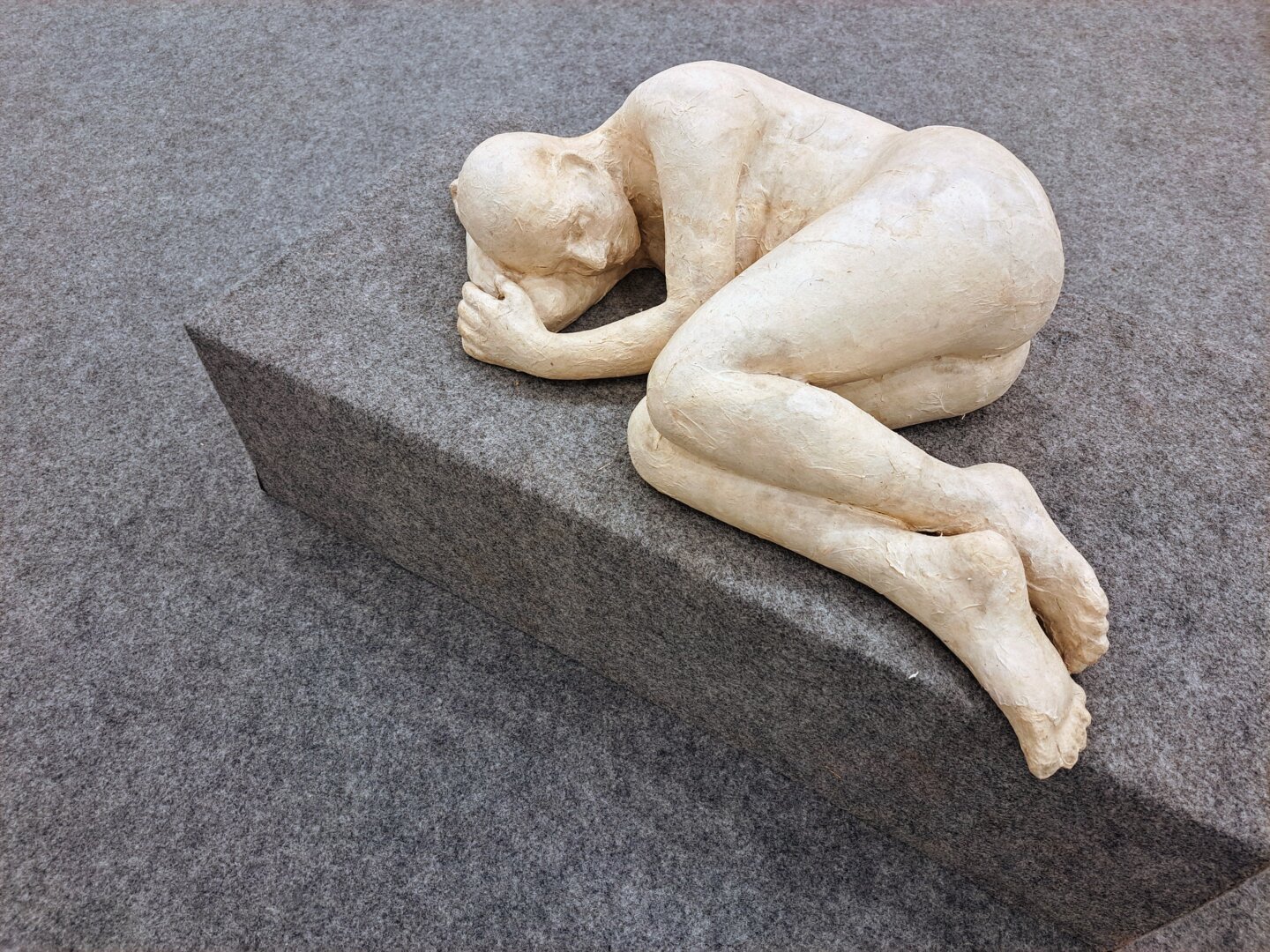 Clay Sculpture of a man sleeping on a foetal position without his clothes. Hand below his head.