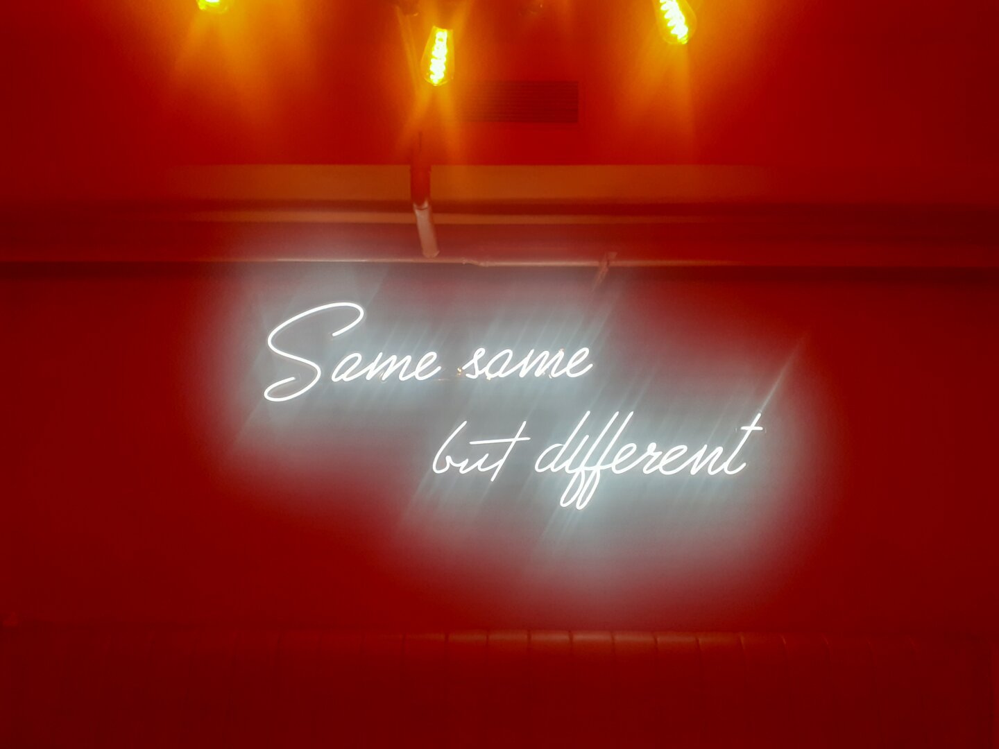 Sign in a cafe with red light ambience that says Same same but different.