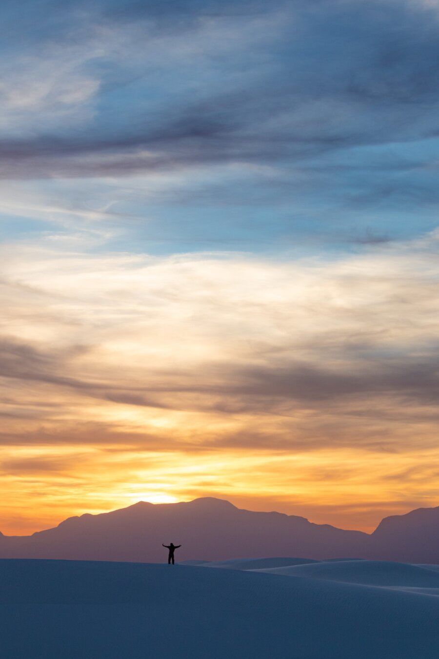 A man on a dune is overwhelmed by a sunset at White Sands National Park.