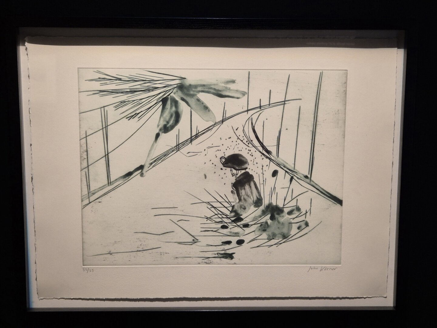 A framed black-and-white print depicts a small solitary figure sitting near a winding road lined with tall vertical trees. Loose ink washes and energetic lines suggest pine branches overhead and scattered vegetation, creating a quiet, contemplative atmosphere.