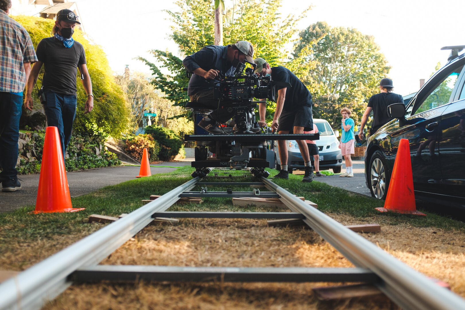 Foreground of Dolly track leads us to a Dolly with the cinematographer adjusting the camera. Crew members walk on either side of the Dolly