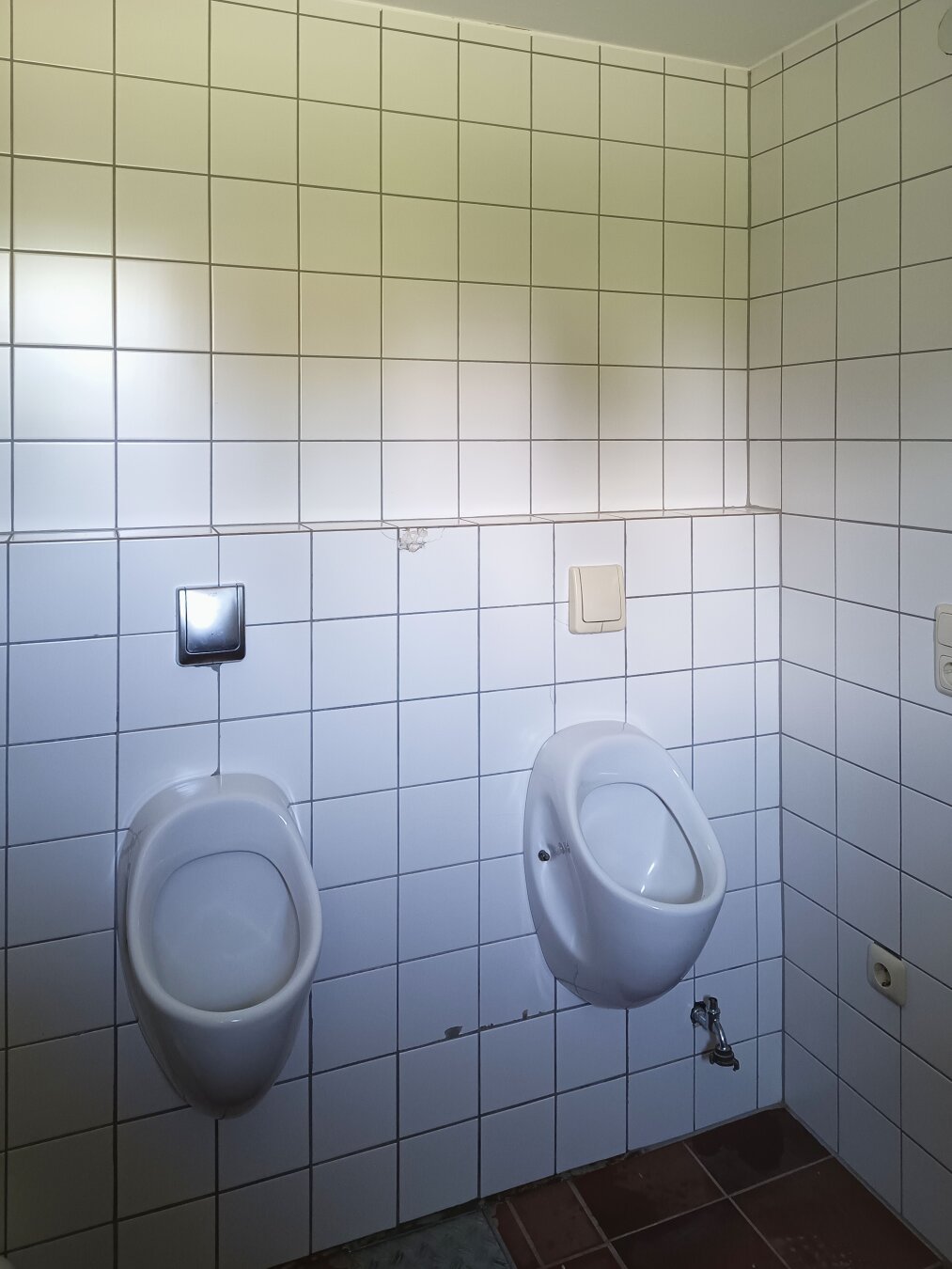 Two white urinals on a tiled wall in a restroom. The somewhat used but clean, orderly setting conveys a utilitarian, hygienic atmosphere.