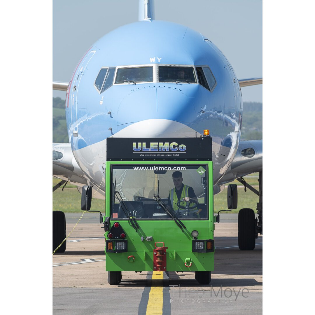 A hydrogen-powered aircraft tug pulls a Boeing 737 onto a stand at Exeter Airport