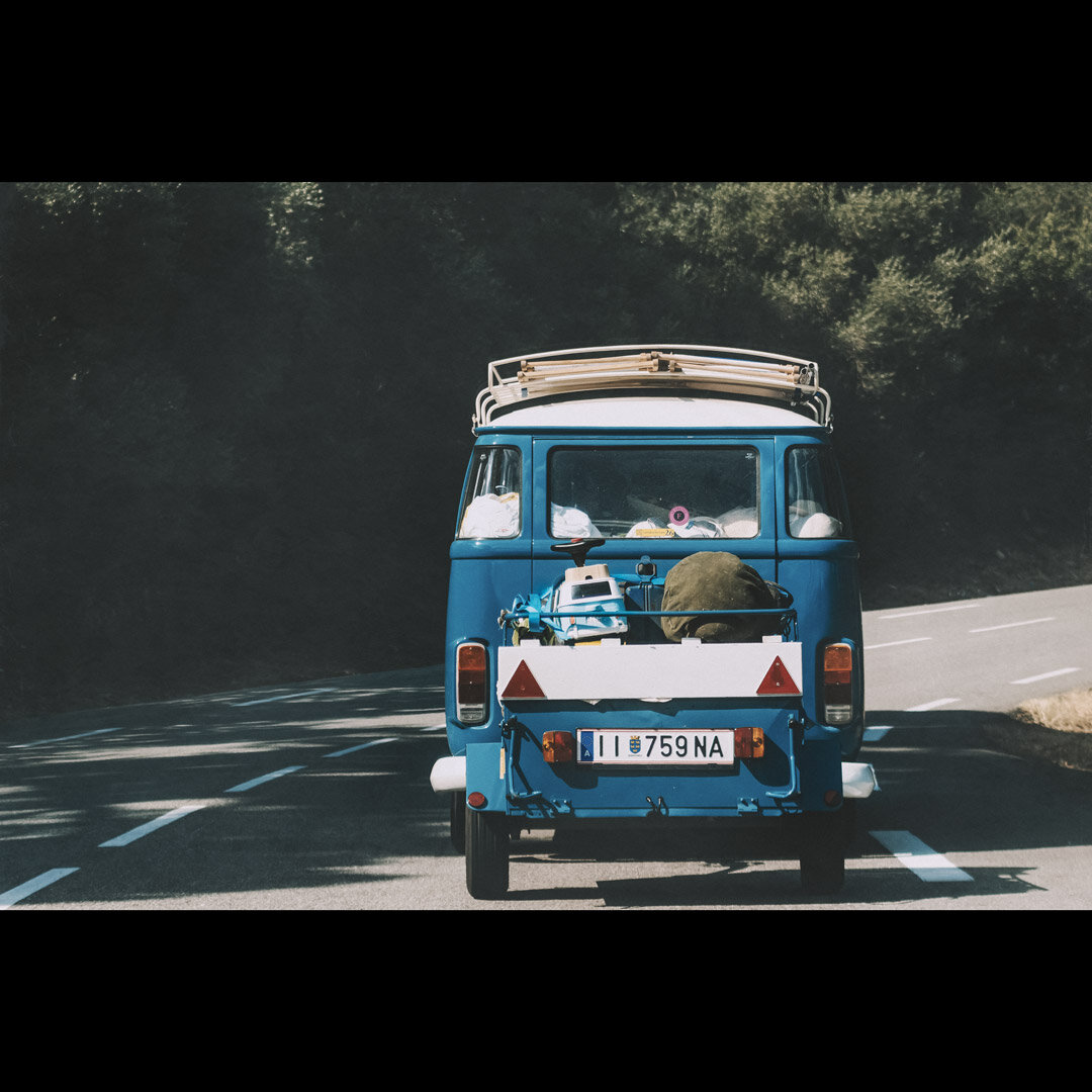 On an italian road, a blue van with a little baby blue van in the trunk behind
