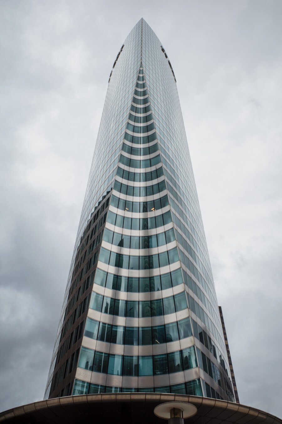A towering skyscraper in La Défense, Paris, with a sleek, curved glass facade that reflects the cloudy sky. The shot, taken from below, emphasizes the height and futuristic design of the building.