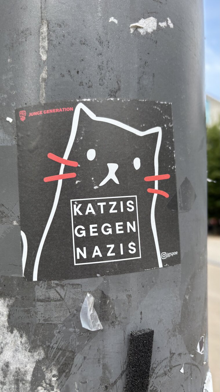 Ein Aufkleber auf einem Laternenpfahl. Abgebildet sind die groben Umrisse einer Katze, darunter die Zeilen „Katzis gegen Nazis“