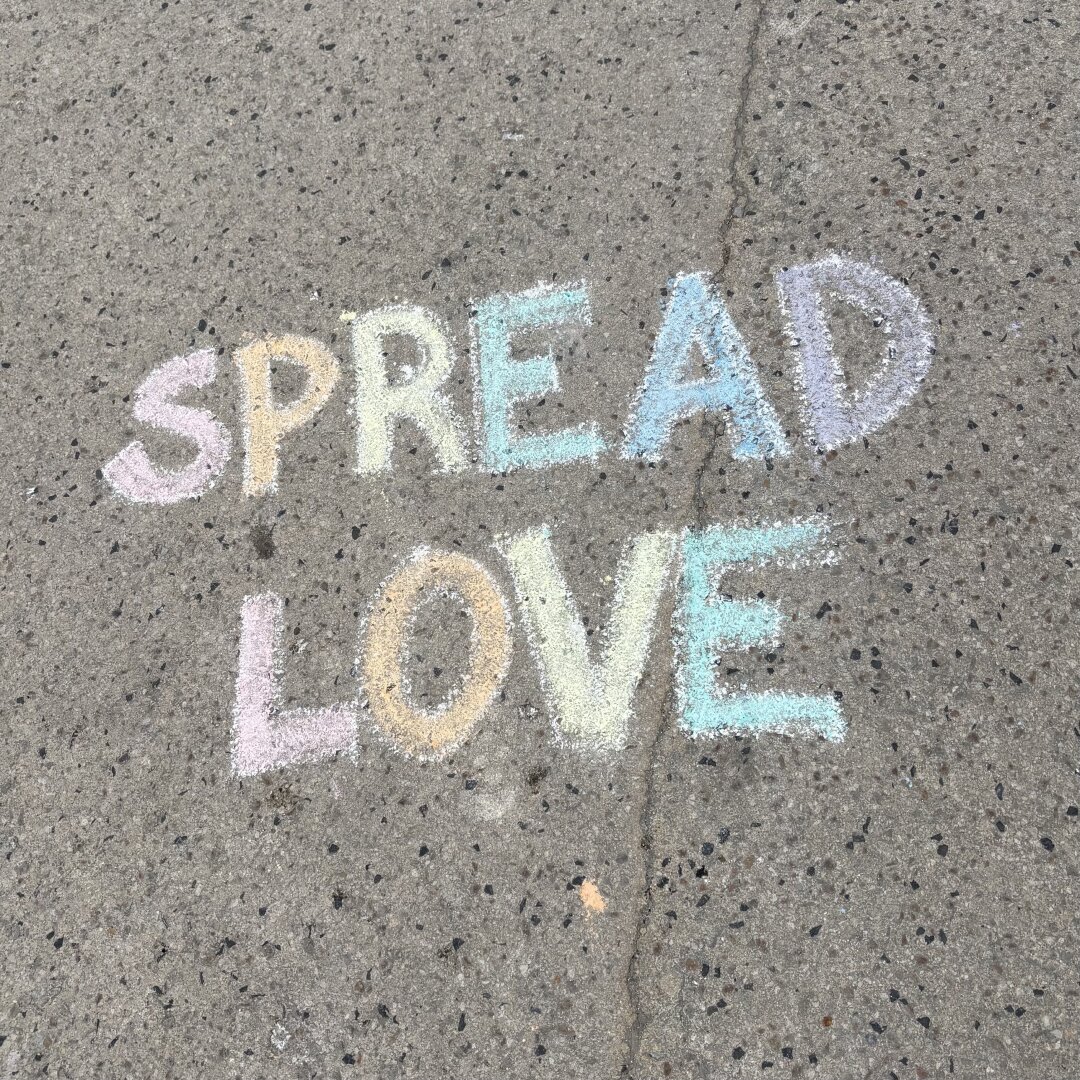 Jemand hat mit bunten Kreiden SPREAD LOVE auf die Straße gemalt