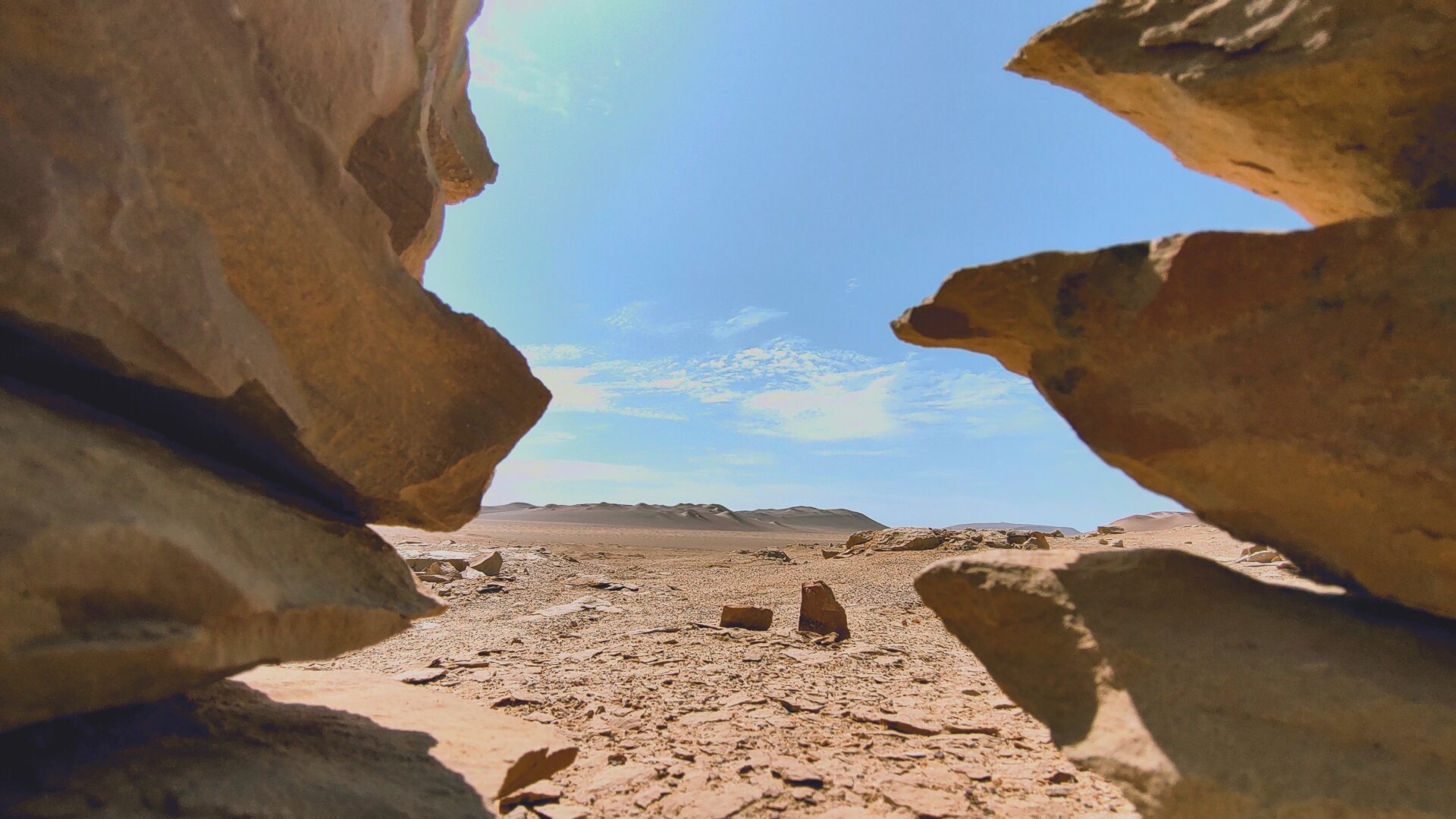 A view through two of the little piled-up stone towers onto the expanse of the desert landscape.
The angle of view has been chosen so that the perhaps knee-high towers on the left and right edges of the picture make the view look as if it is through a ravine.