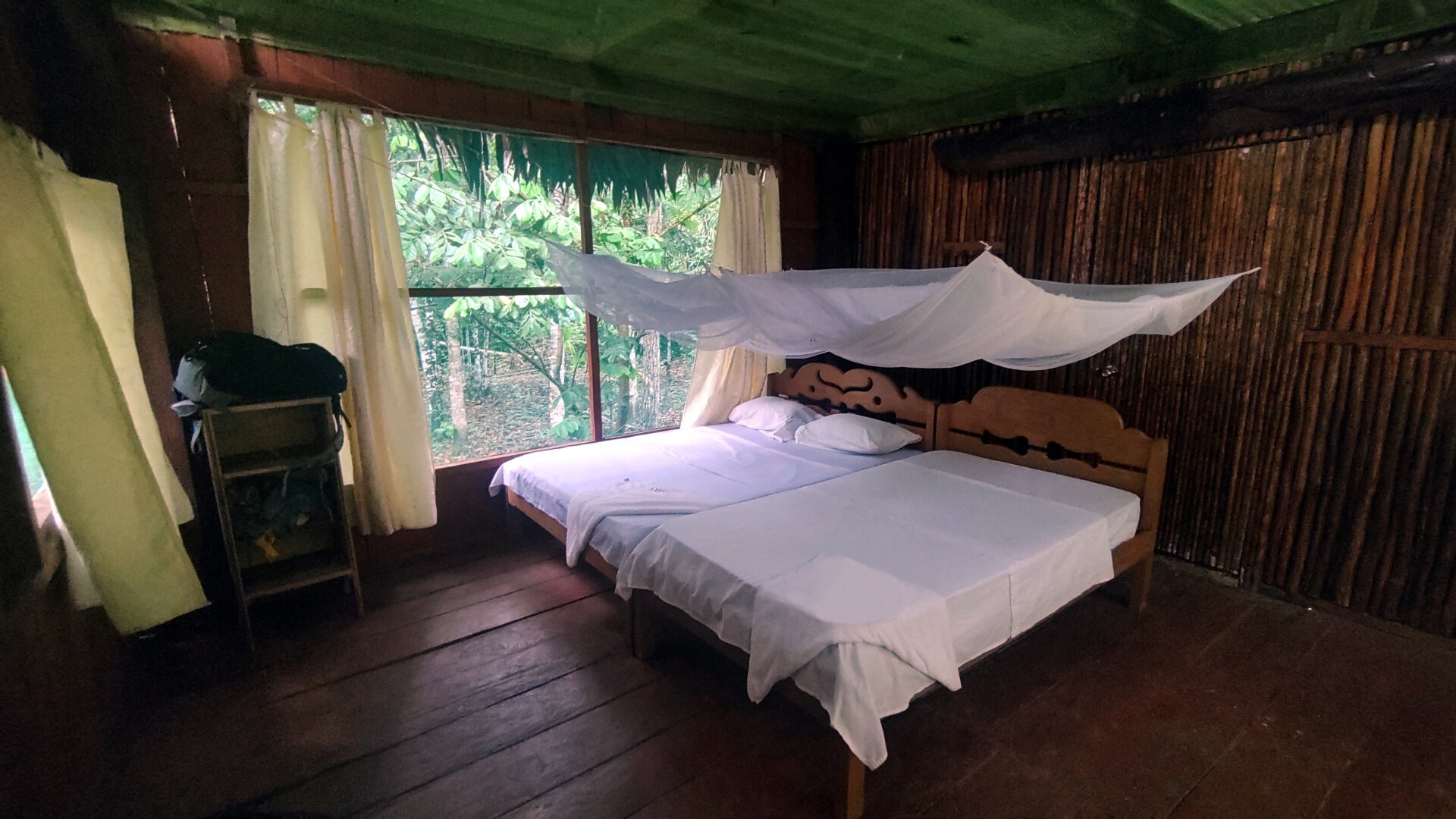 The inside of the wooden cabin. A large king-size bed is freshly made up with bright white linen sheets. A white mosquito net is strung over the bed.