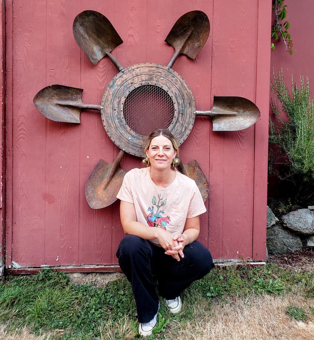 Vancouver Island artist, Leslie Love, outside crouching beneath her sculpture.