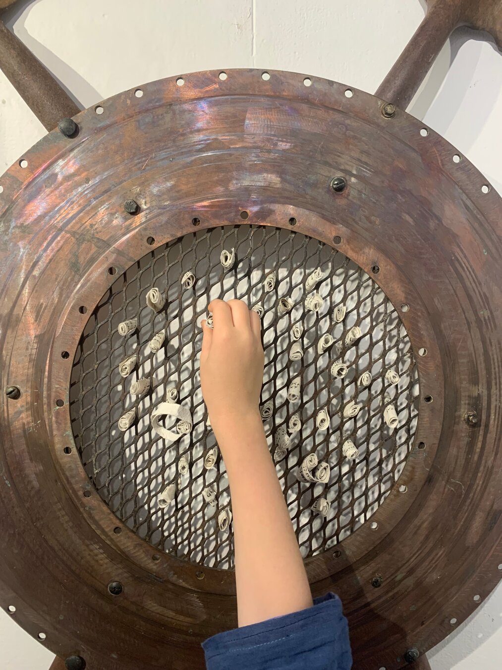 A child's hand takes a paper "seed" from a copper and scrap metal sculpture of a sunflower.