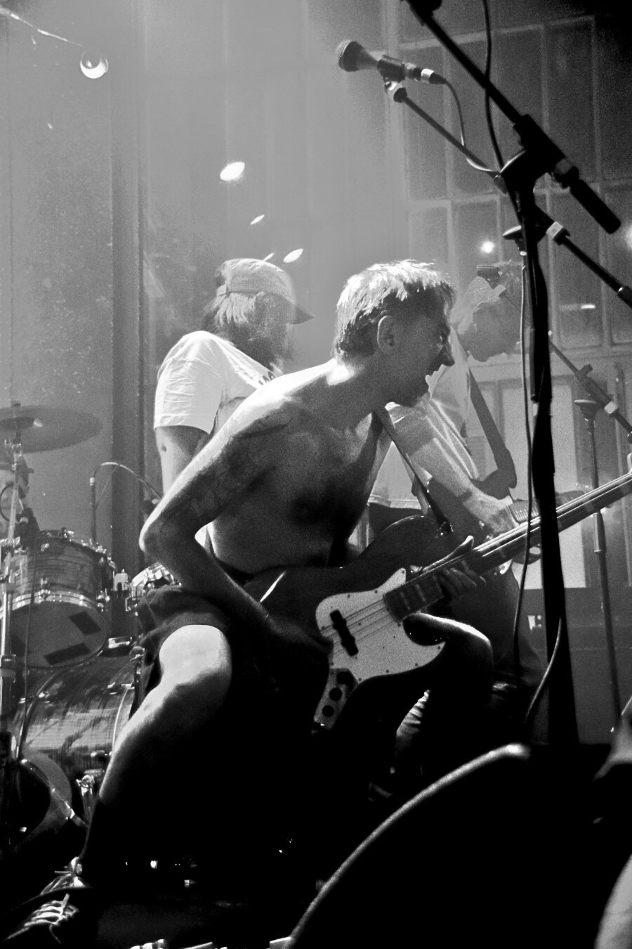 Groupe sur scène, photo noir et blanc, au premier plan le bassiste en jupe et torse nu qui harangue la foule