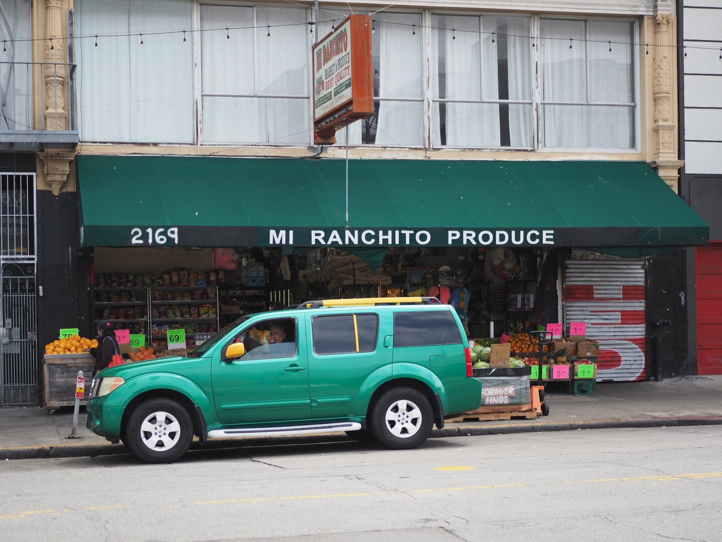 A bright green car in front of a grocery store with a green awning