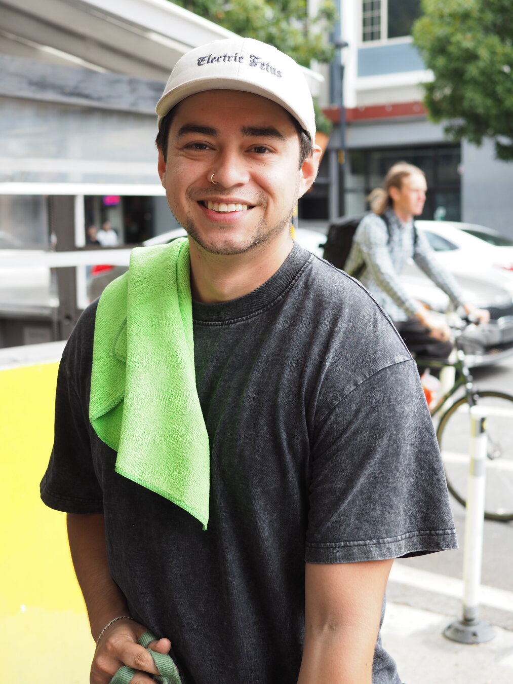 A street portrait of a smiling young man with a bright green cloth over his shoulder (he was walking a puppy)