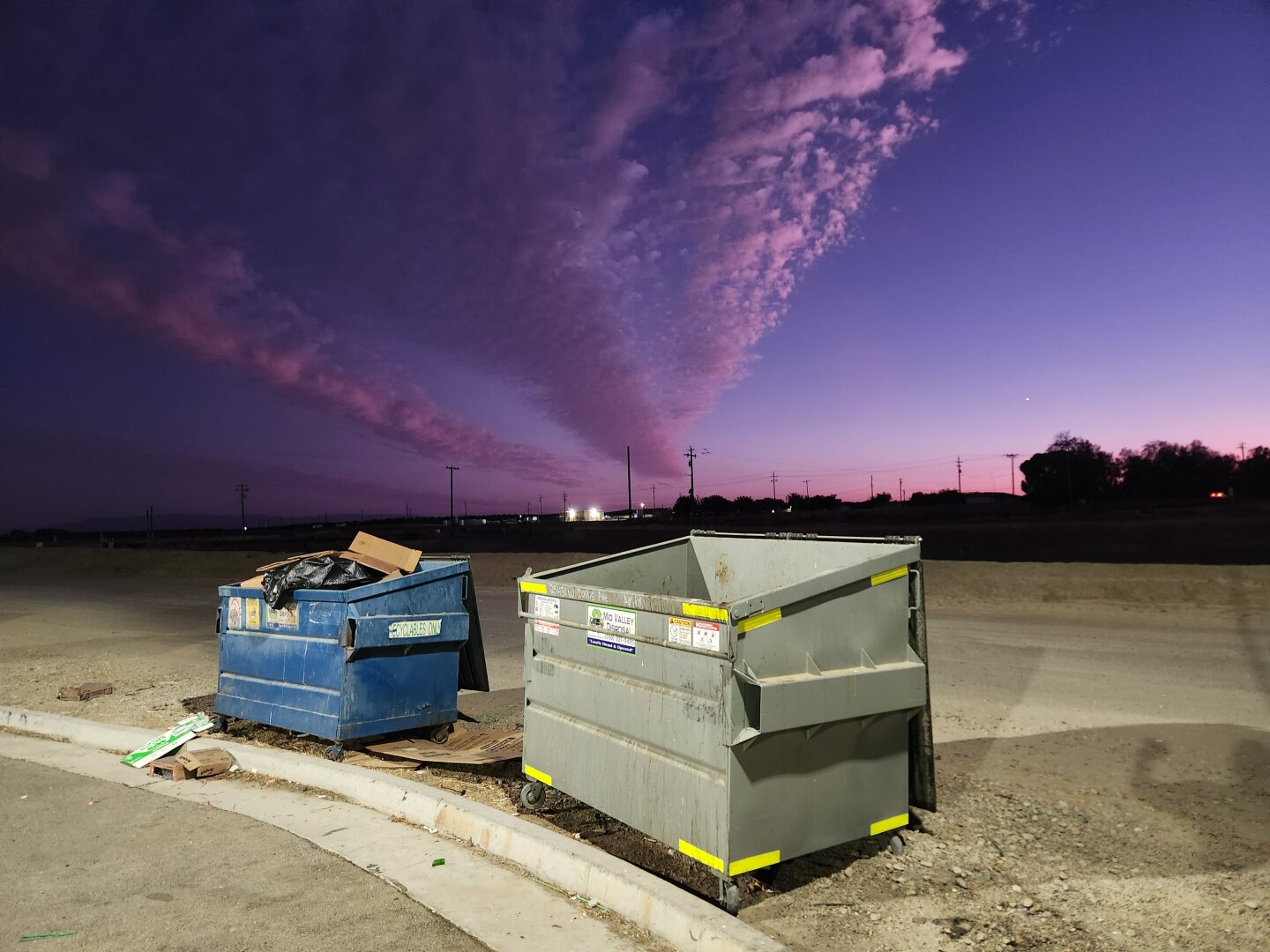 A photo of two dumpsters in the foreground, with a blue and purple cloudy sunset
