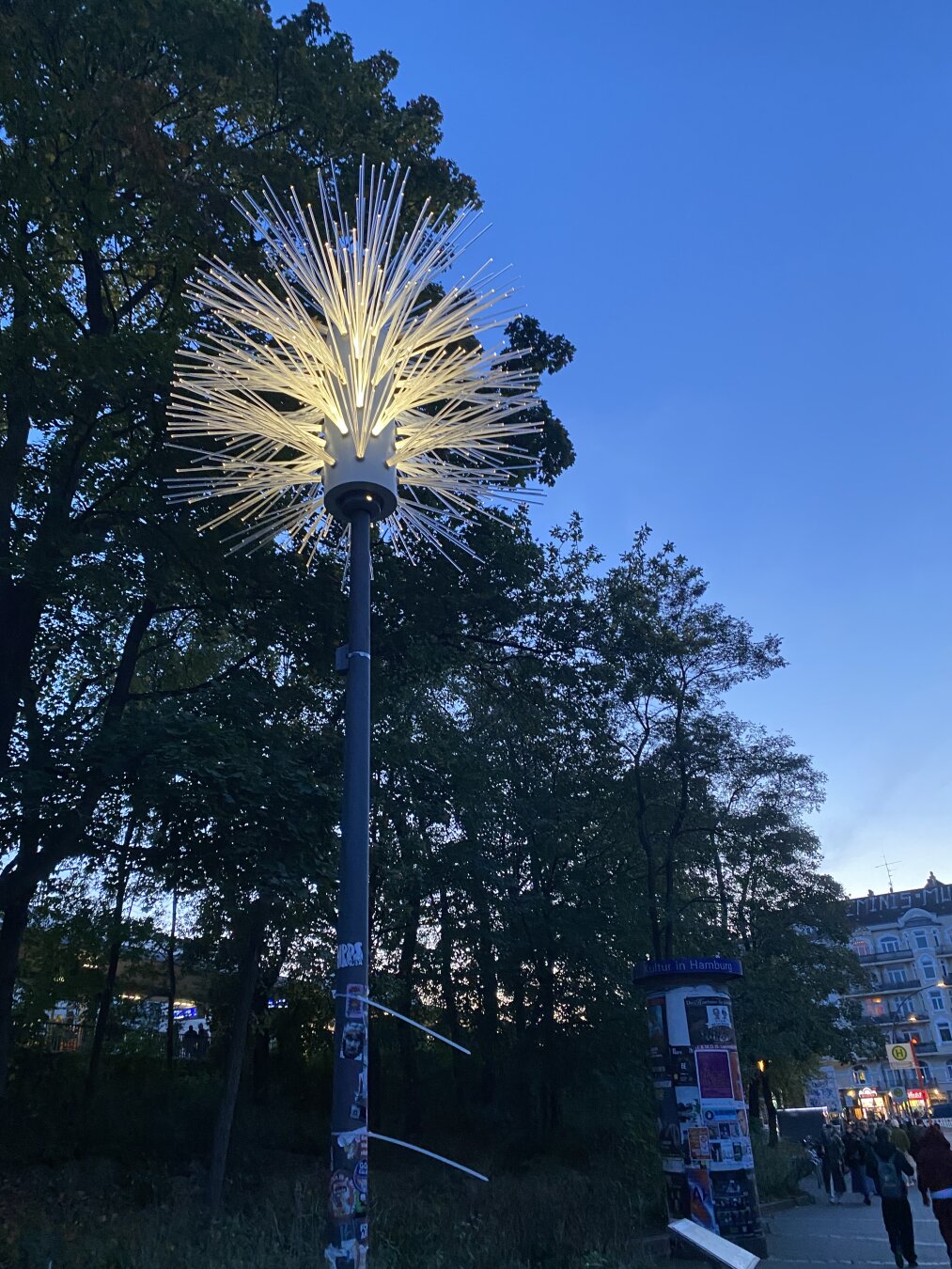 A lit xxl toilet brush on a lamp post. Trees in the background