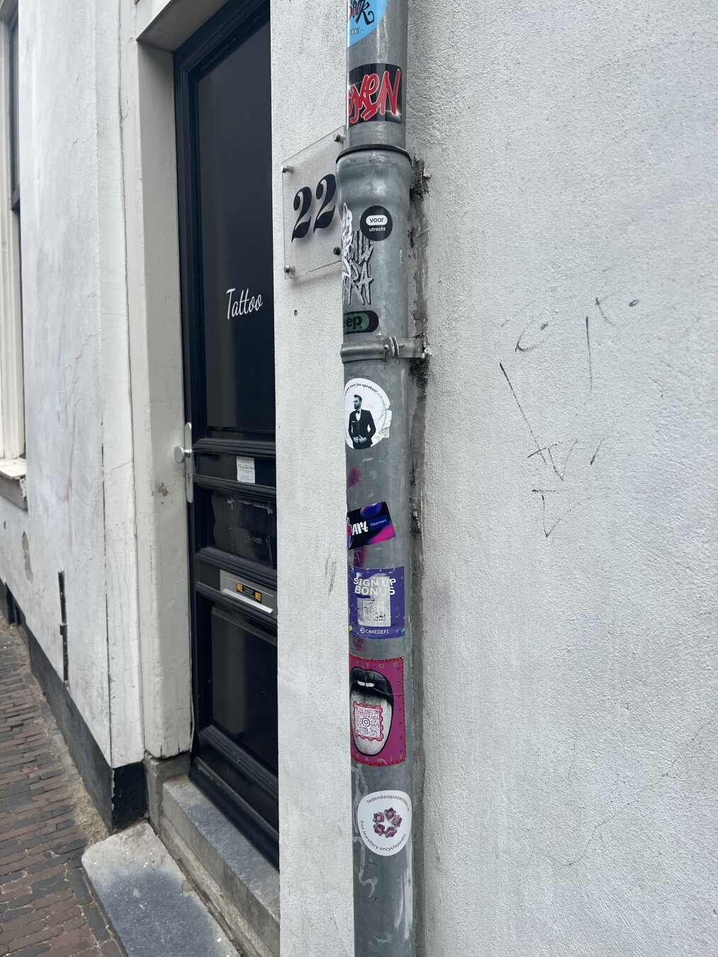 Ronde sticker van hedendaagsesieraden.nl onder andere stickers op een grijze regenpijp naast een deur.