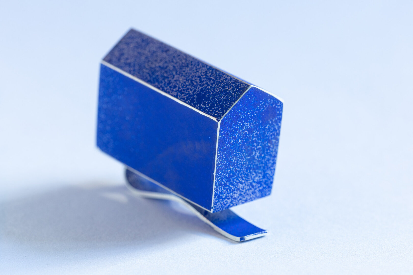 Reverssieraad van zilver, een gestileerde vorm van een huis in blauw op een schuif.