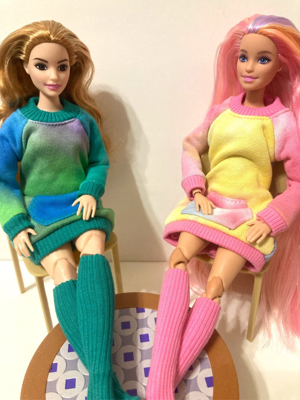Two Made to Move Barbies are shown in oversized sweatshirt dresses and matching knee-high socks. On the left, curvy floral pants yoga in green and blue, and on the right, a hair play hybrid Millie doll in pink and yellow.