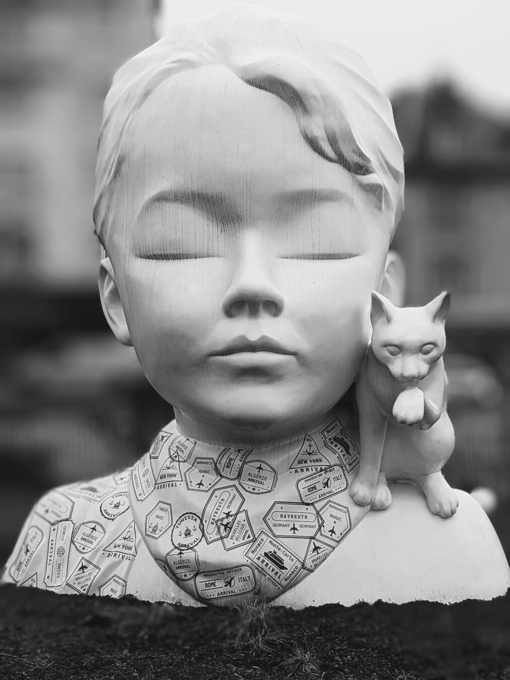 Skulpture of a girl's head with eyes closed, she has a cat on her shoulder. the background is blurred, black/white