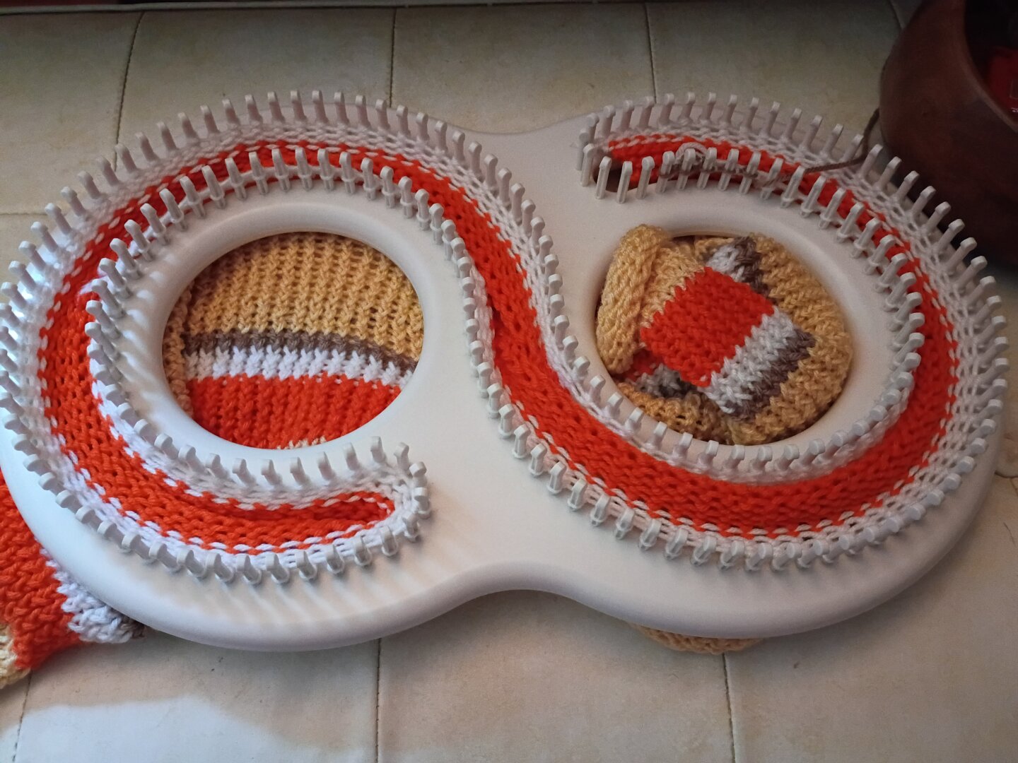 Blanket in progress on an infinity loom. 16 rows yellow, 8 rows orange, 4 rows white, 2 rows brown in a repeating pattern.