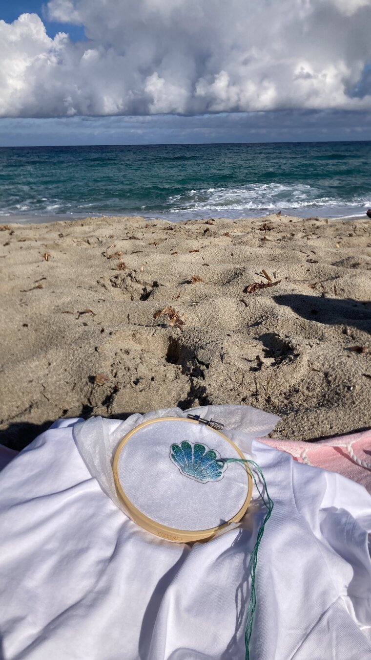 Même vue de la plage avec en premier plan le t-shirt blanc sur lequel je brode un coquillage dans un dégradé de bleus allant vers le vert d’eau.
