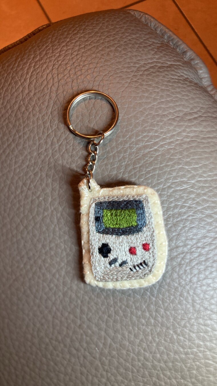 Une game boy brodée, montée en porte-clefs, posée sur un accoudoir en cuir gris