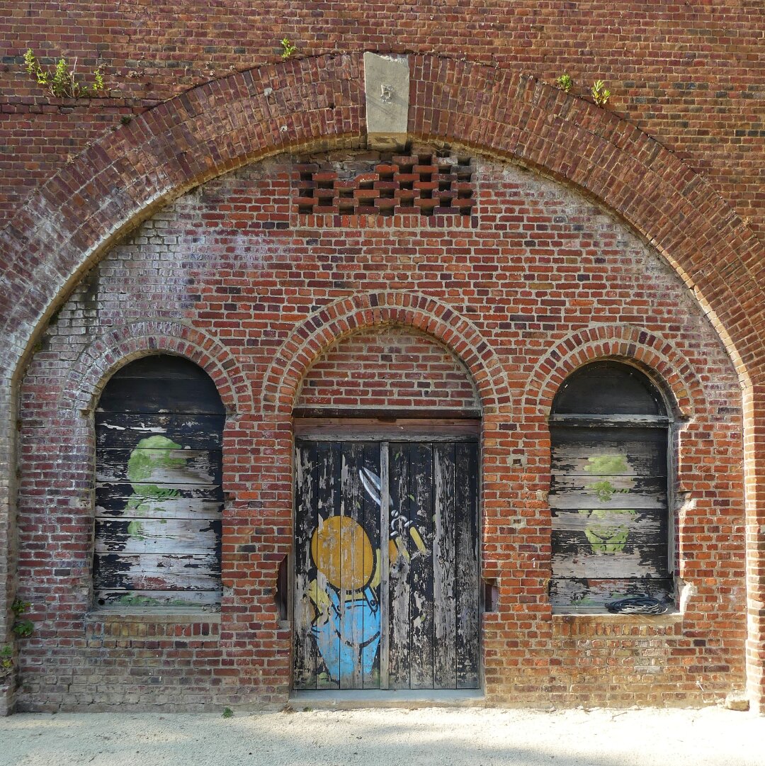 Du streetart est peint sur une vieille porte et des vieux volets en bois. Le mur est en brique avec des formes arrondi